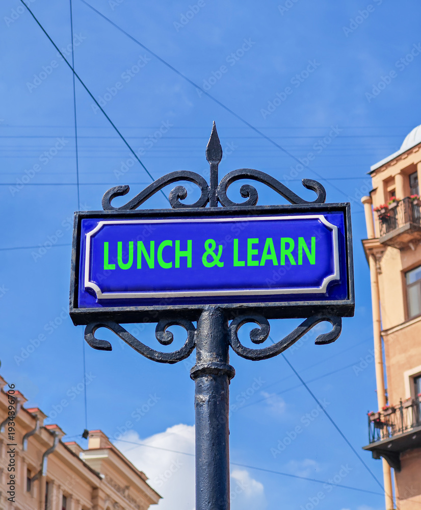 Fototapeta premium Lunch and learn symbol. Concept words Lunch and learn on beautiful big blue road sign. Beautiful blue sky and buildings background. Business, educational and lunch and learn concept. Copy space.