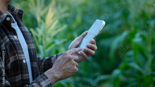 Cropped view of the optimistic farmer scientist in plaid shirt using smartphone mobile technology application while working at the field