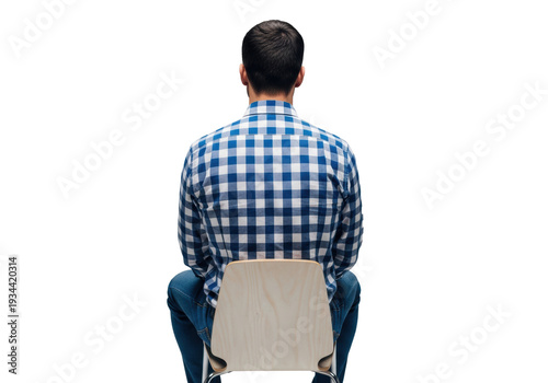 Adult caucasian man with short dark hair in a plaid shirt and jeans sitting on a wooden chair from the back in a studio concept of quiet contemplation