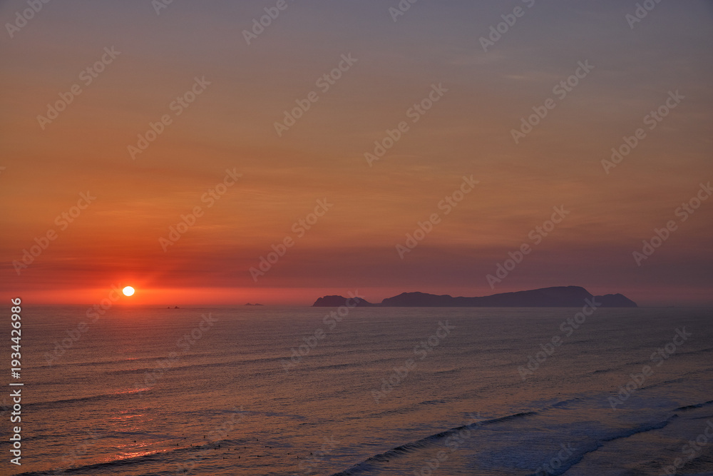 Fototapeta premium Golden sunset over the Pacific Ocean viewed from the Malecón in Miraflores, Lima, with San Lorenzo Island on the horizon. Scenic coastal landscape promoting active lifestyle, wellness