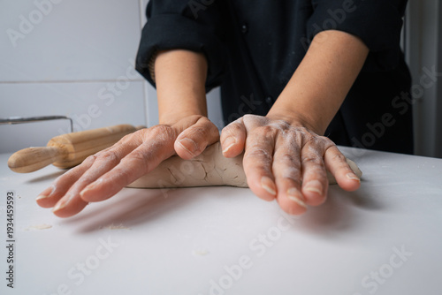Close-up of an unrecognizable person kneading bread dough with their hands on a floured countertop using a rolling pin