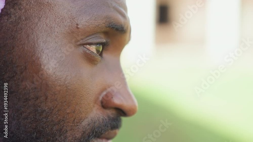 Male athlete profile closeup outdoors intense gaze bearded man side view sweating after training sunlight on textured skin blurred green background runner taking recovery pause thoughtful expression