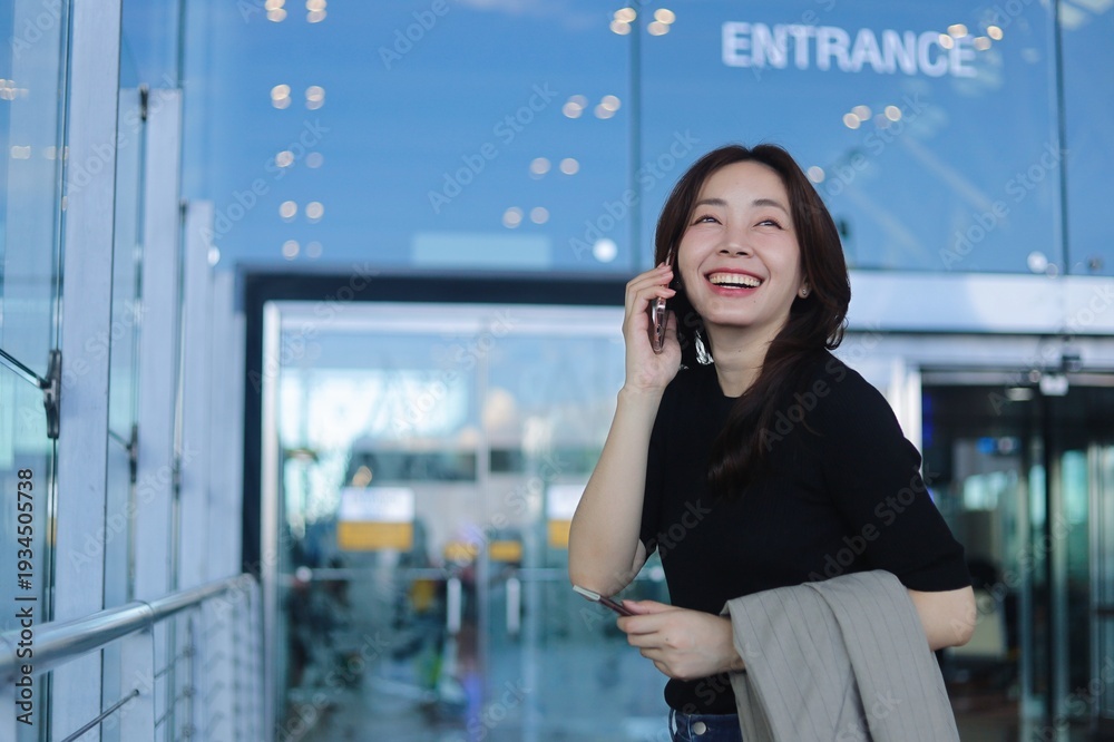 Fototapeta premium Smiling young Asian woman holding passport inside modern airport terminal. Concept of international travel, business trip, relocation.