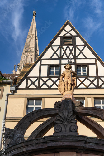 Portrait view of the statue on the Staupen Fountain (Market Fountain) at the market square opposite the Old Town Hall in Merseburg, Germany, with half-timbered houses and the city church roof in the b
