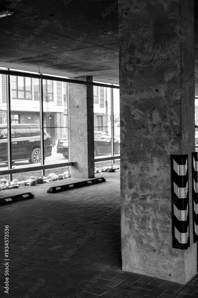 Fototapeta premium Concrete pillar in modern parking garage with large windows and vehicles