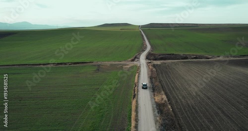 One black suv car driving alone, travel on empty straight asphalt road through agriculture fields at summer sunny day. Aerial drone wide view