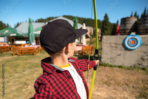 Portrait boy holding bow shooting target mountain field. Sunny summer day forest hills scenery. Outdoor games kids. Archery training summer camp. Active childhood development travel leisure hobby conc