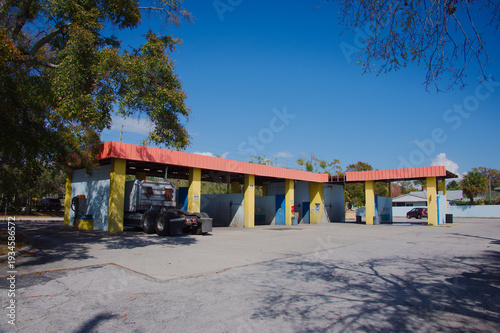 Wallpaper Mural Abandoned car wash bays with a parked semi truck under a bright blue sky, surrounded by trees and empty pavement, conveying a calm, nostalgic roadside atmosphere in a suburban setting.
 Torontodigital.ca
