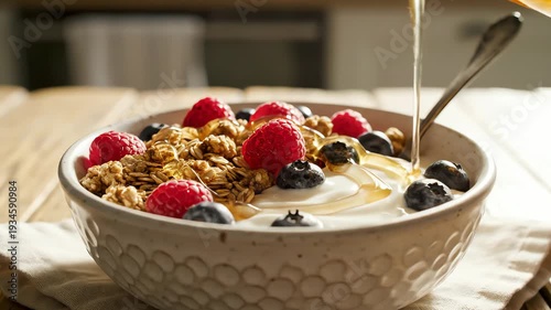 Close up of a bowl of granola with berries and honey on a wooden table