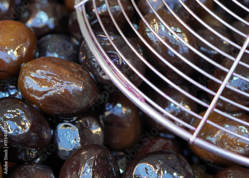 Close-up of glossy black olives in oil with a metal spider strainer, highlighting the rich texture and traditional Mediterranean food preparation
