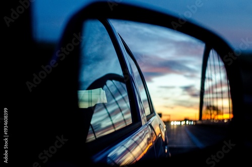 Viewing a dramatic sunset and city lights reflected in a car side mirror
