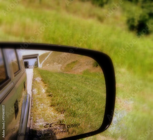 View reflecting a rural road, grassy shoulder, and bridge in a vehicle's side mirror.
