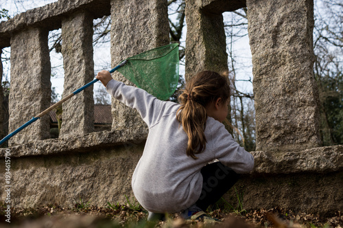 Foto Back view of a young explorer with a net, investigating the gaps in a stone fence during a sunny day outdoors