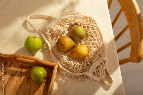 Eco mesh bag with ripe pears on wooden table in natural sunlight, rustic summer kitchen mood