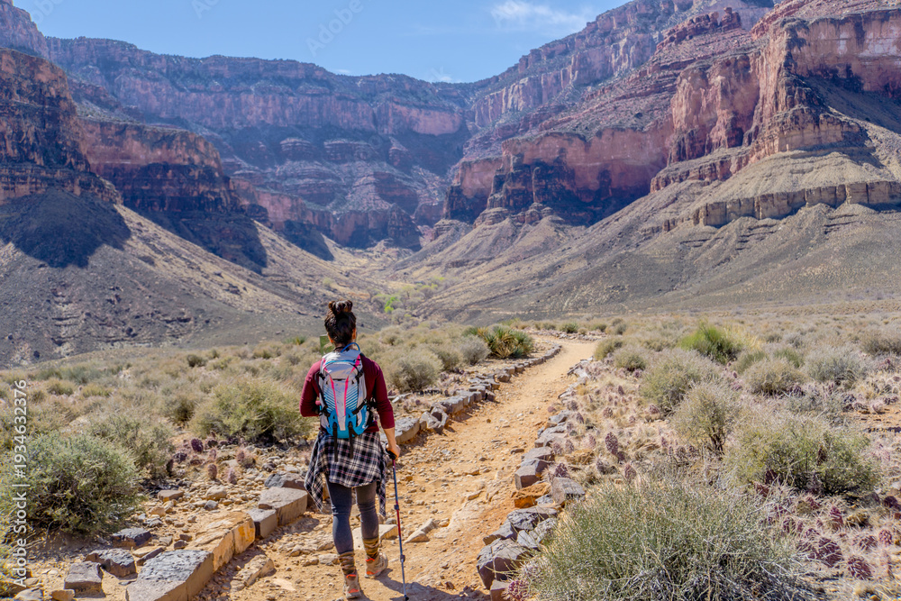 Fototapeta premium A woman is walking down a dirt road in the desert