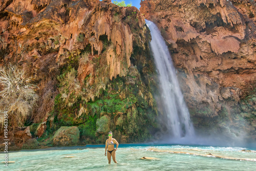 A woman stands in front of a waterfall, taking a picture