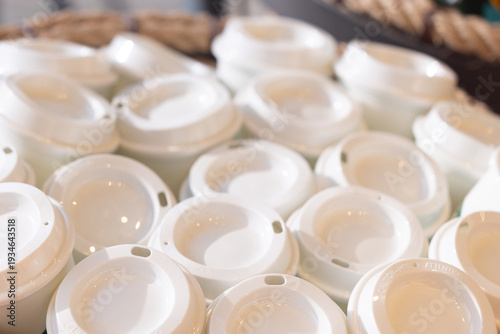 Stack of white plastic coffee cups with white lids in basket reusable cups