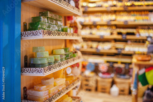 Colorful handmade soap bars displayed on wooden shelves in a shop, with various products and decor visible in the blurred background