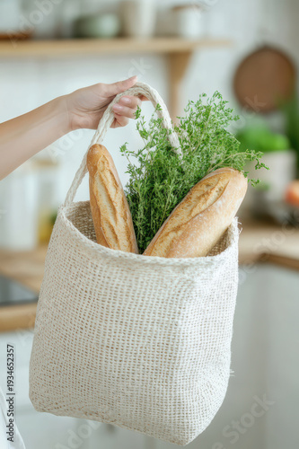 Fresh bread and herbs in a woven bag held in a kitchen setting