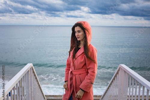 a girl in a coral coat against the backdrop of the sea in autumn