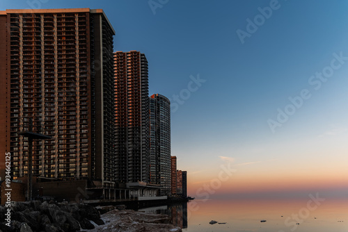 Evening cityscape with tall buildings on the shore of Lake Michigan with the horizon blurred by the setting sun.