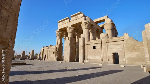 Kom Ombo temple ruins with double columns and composite capitals against clear blue sky in Egypt, ancient Ptolemaic architecture dedicated to Sobek and Horus with damaged walls.