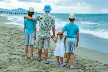 Happy large family standing on sandy beach, looking out ocean waves together, father grandfather with children observing waves, family bonding during summer beach holiday getaway, school holidays