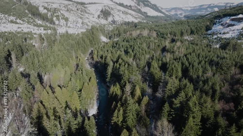 Aerial drone footage over a mountain forest and river setting with clear cutting in winter.