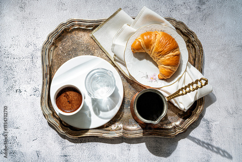 A cup of coffee, fresh croissant,coffee pot on a table with sunlight. Table set for breackfast. Flat lay.