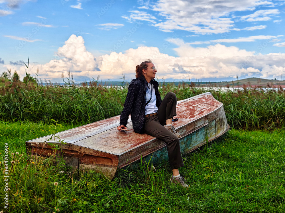 Fototapeta premium Middle aged woman relaxes on a weathered boat in a serene natural landscape during a clear day