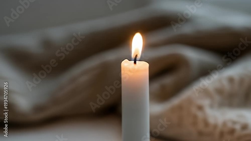 A close-up shot of a lit candle with a soft, blurred background of a knitted blanket, creating a cozy and warm atmosphere.