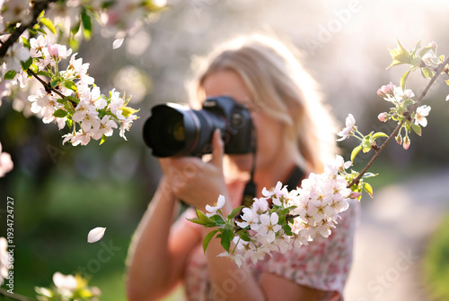 Blonde woman photographer taking pictures of blooming spring trees with a professional camera. Authentic lifestyle imagery ideal for photography education, travel, and seasonal marketing.