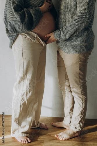 Stylish pregnant couple hugging baby bump close up. Fertility, health care and expecting new life concept. Happy Mothers day. Family in cozy sweaters and jeans holding pregnant belly