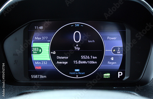 Electric car speedometer. Moder car dashboard. Close-up view vehicle digital driver display. Black circular screen shows speed, 2 kW power draw, 283 km range bar in green, 15.8 kWh average efficiency,