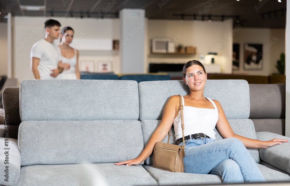 Obraz premium Glad young female customer viewing sofas during shopping in furniture store