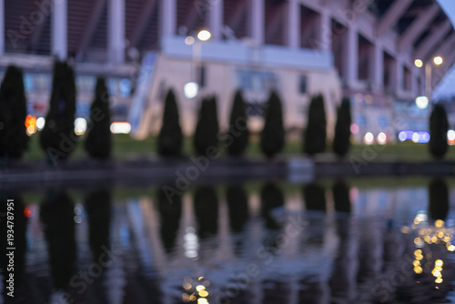 Wallpaper Mural out of focus evening shot of a modern stadium reflected in a calm lake with silhouettes of trees and glowing city lights creating a beautiful bokeh effect Torontodigital.ca