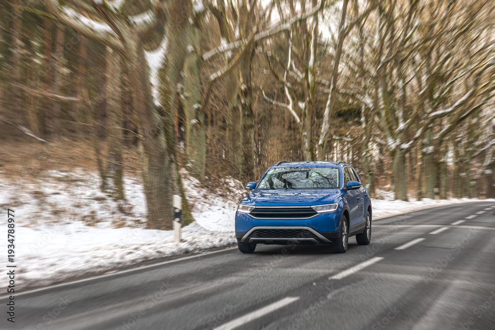 Fototapeta premium Blue crossover driving on snowy forest road. Winter car travel.