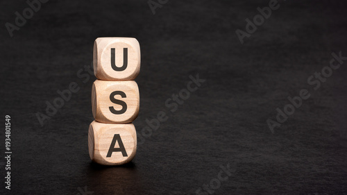 USA word on wooden blocks stacked vertically on a dark black background. Concept of United States economy, patriotism, American business and politics.