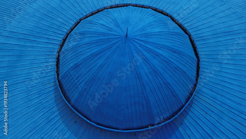 Top-down drone shot of a circular blue water storage tank overlooking an urban community in a tropical city.