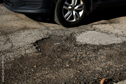 Car Tire Navigating Dangerous Potholes on Severely Damaged Asphalt Road