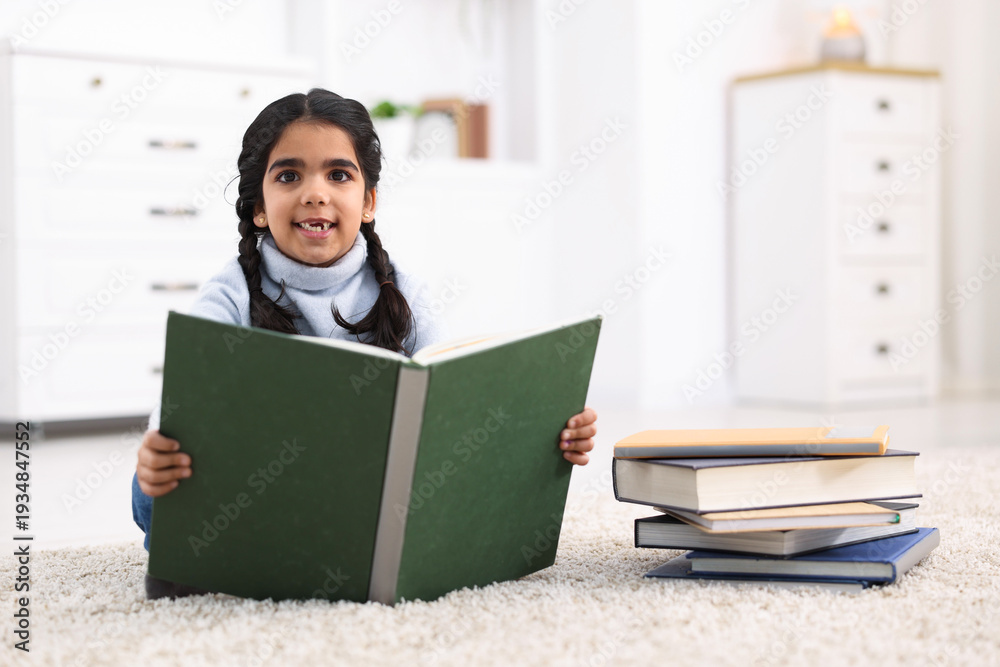 Naklejka premium Cute little girl reading book on floor at home. Space for text