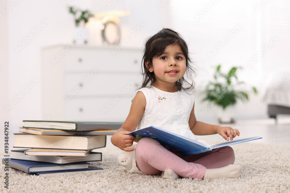 Naklejka premium Cute little girl reading book on floor at home. Space for text