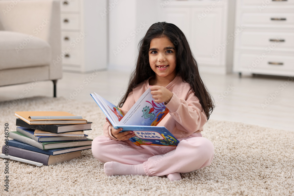 Naklejka premium Cute little girl reading book on floor at home