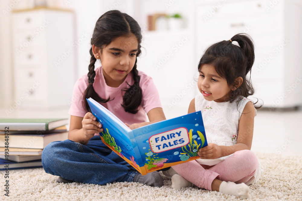 Naklejka premium Cute little girls reading book together at home