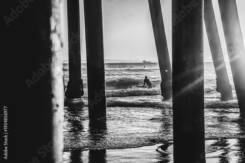 Black and white view of a surfer through the Huntington Beach Pier in Huntington Beach, California