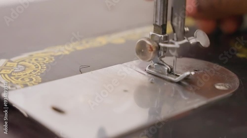 Closeup black sewing machine presser foot showing hand guiding fabric and needle through ornate gold bed steady stitching, small household repair chore in quiet home, vintage metal plate and delicate