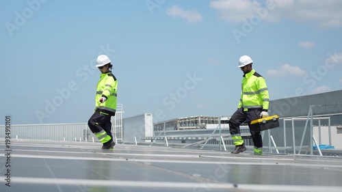 Solar energy specialists in high-visibility gear walking on rooftop during site inspection, Industrial technicians pointing and coordinating renewable energy project installation