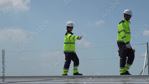 Engineering team in safety gear supervising photovoltaic system installation on industrial roof, Solar energy technicians with toolbox and clipboard walking on rooftop for inspection and maintenance