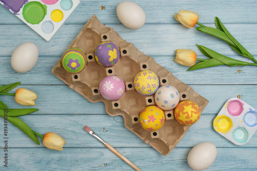 Obraz premium Easter Crafting. Decorated eggs in an egg carton with tulips on a wooden background.