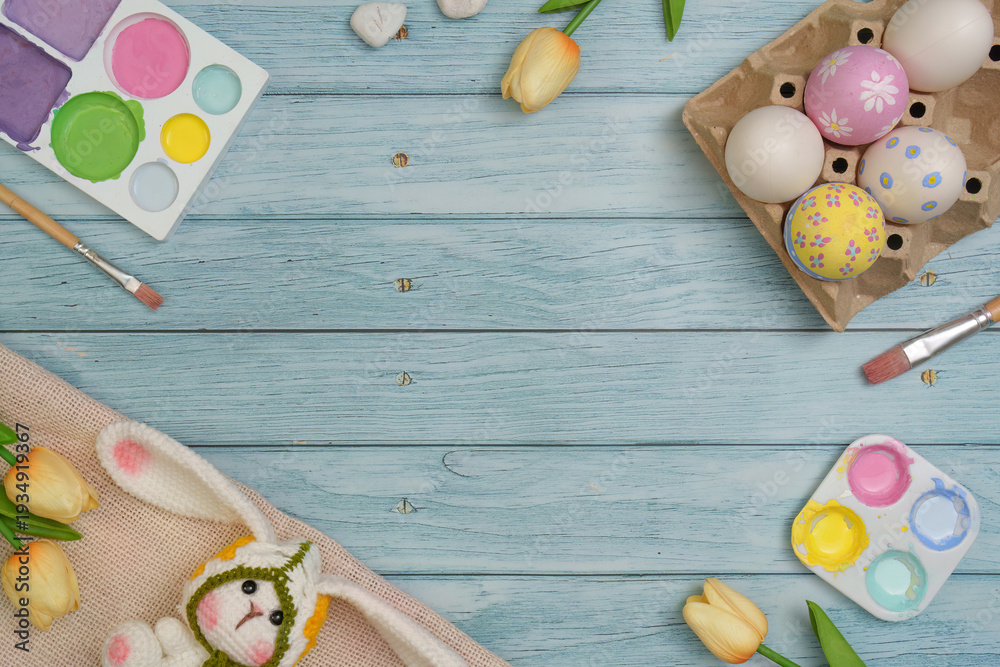 Fototapeta premium Easter Fun. Colorful eggs and a bunny toy on a wooden table with paint supplies.